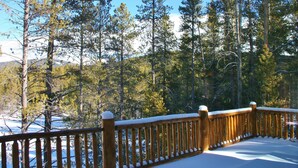 A wooden deck with snow-covered railings overlooking a forested area with tall trees and a mountain in the background. - Bear's Den-Pet Friendly! Close to Ski Cooper.  Private lake access! (Leadville)