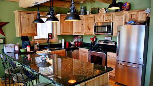 A kitchen with wooden cabinets, a stainless steel refrigerator, a microwave, and a large island with bar stools. - Bear's Den-Pet Friendly! Close to Ski Cooper.  Private lake access! (Leadville)