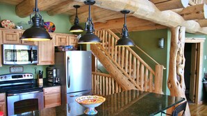 A kitchen with wooden cabinets, a stainless steel refrigerator, a microwave, and a stove. There are hanging pendant lights, a wooden staircase, and a large wooden tree trunk in the corner. - Bear's Den-Pet Friendly! Close to Ski Cooper.  Private lake access! (Leadville)