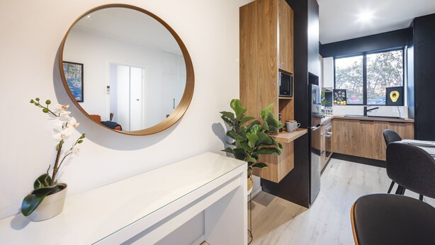 A modern kitchen with a wooden cabinet, a round mirror, and a potted plant. - Jacaranda Apartment | Wayville Walk to Tram (Wayville)