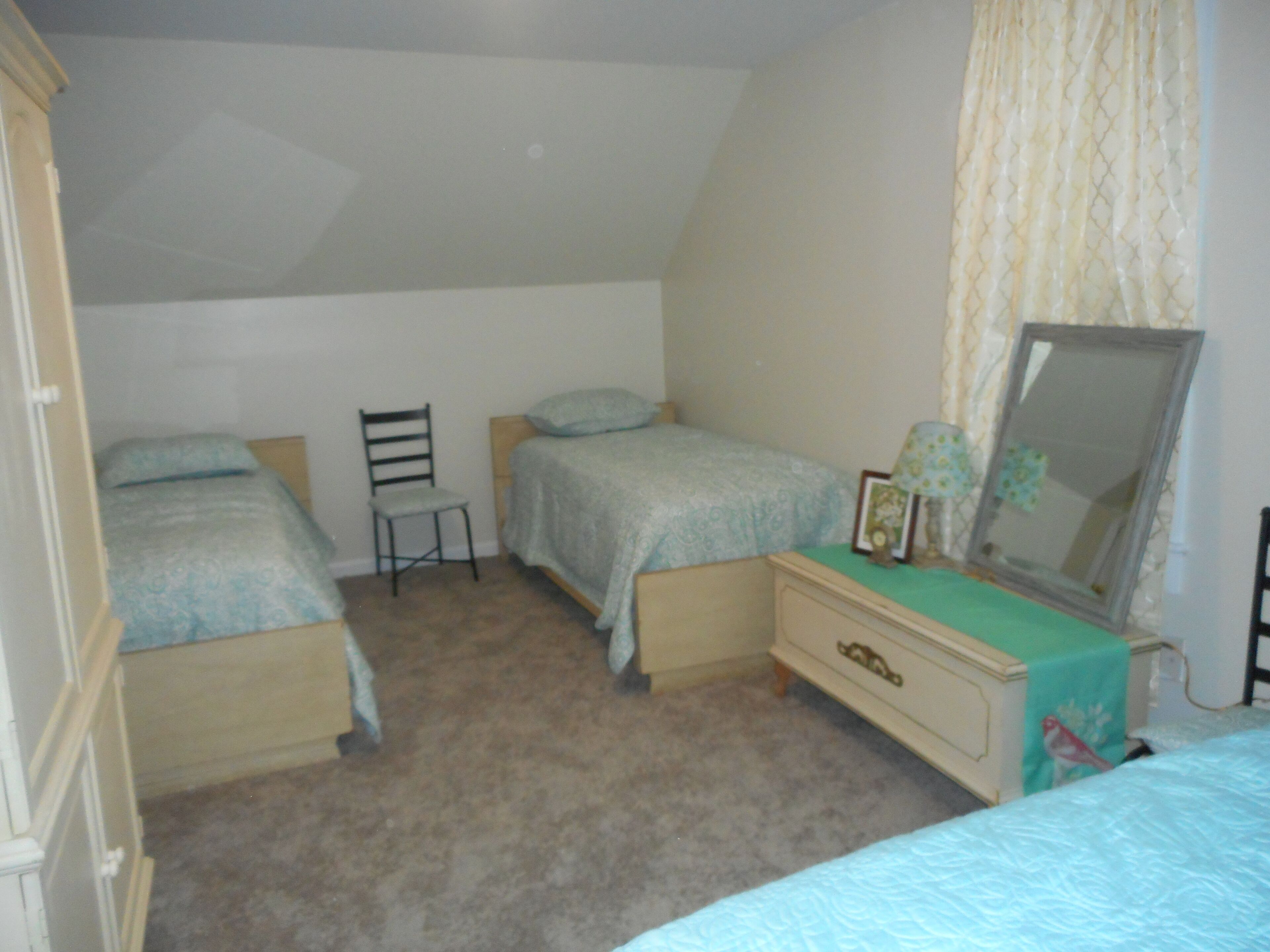 Un dormitorio con dos camas individuales, una silla, un tocador y un espejo.