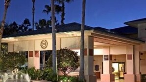 Un hotel con entrada cubierta, palmeras y una fuente.