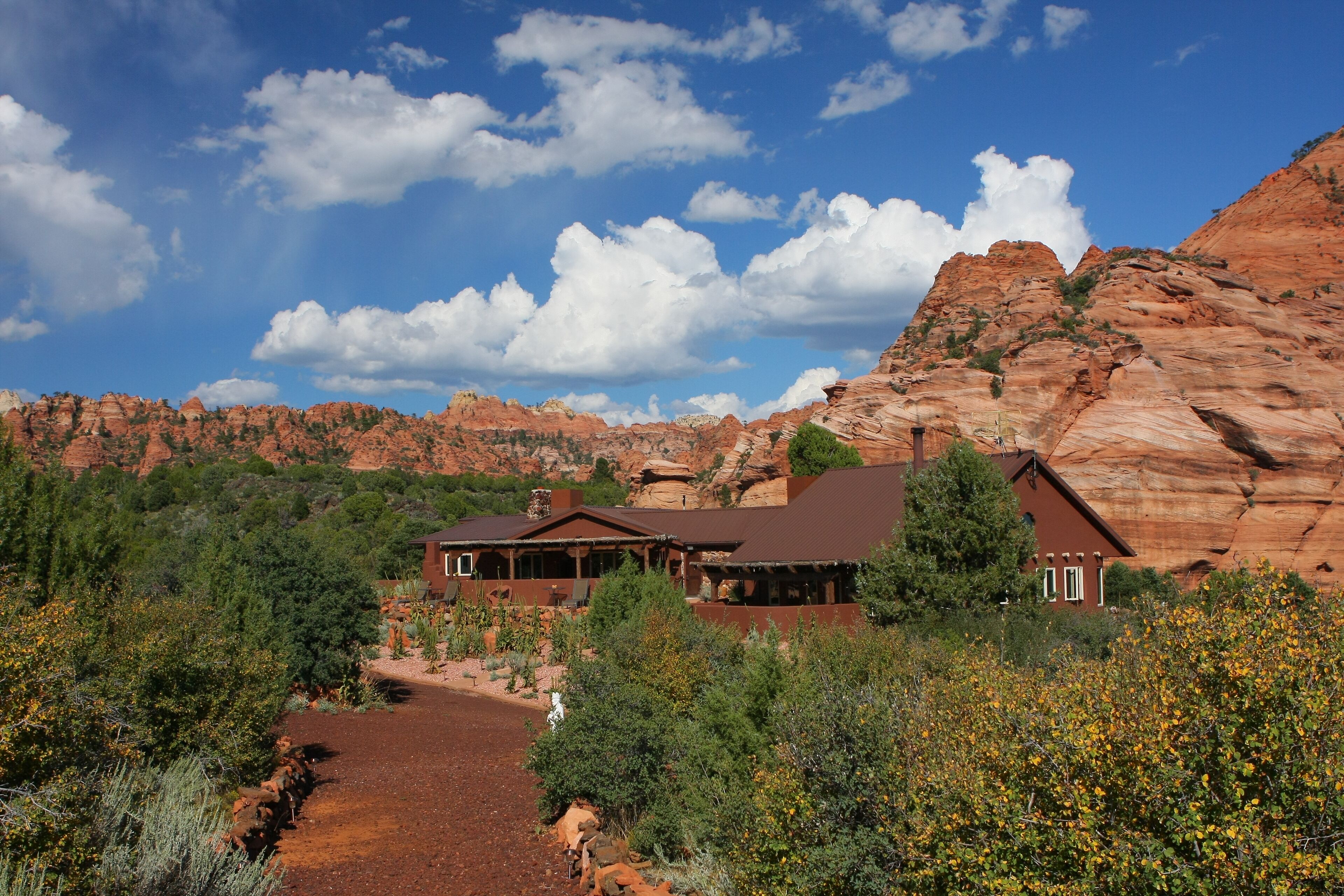 A lodge with multiple rooms, surrounded by red rock formations and greenery.