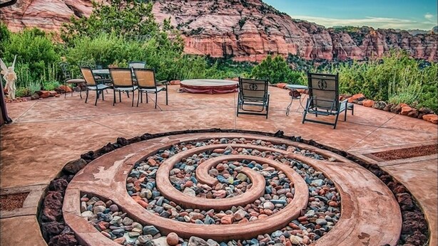 A circular stone fire pit surrounded by outdoor seating, set against a backdrop of red rock formations and a cloudy sky. - Zion Villa/True North:Actually Located in & Surrounded by ZionNP Secluded10Acres (Virgin)