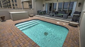 Una piscina en la azotea con agua cristalina, rodeada por un patio de ladrillo. Se observan zonas de estar al aire libre y una parrilla de barbacoa al fondo.