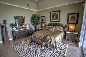 Een slaapkamer met een groot bed, een kaptafel, een stoel, een spiegel en wanddecoratie.