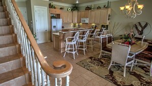Una cocina amplia con una isla central, sillas de mimbre blanco y una mesa de comedor con candelabro.