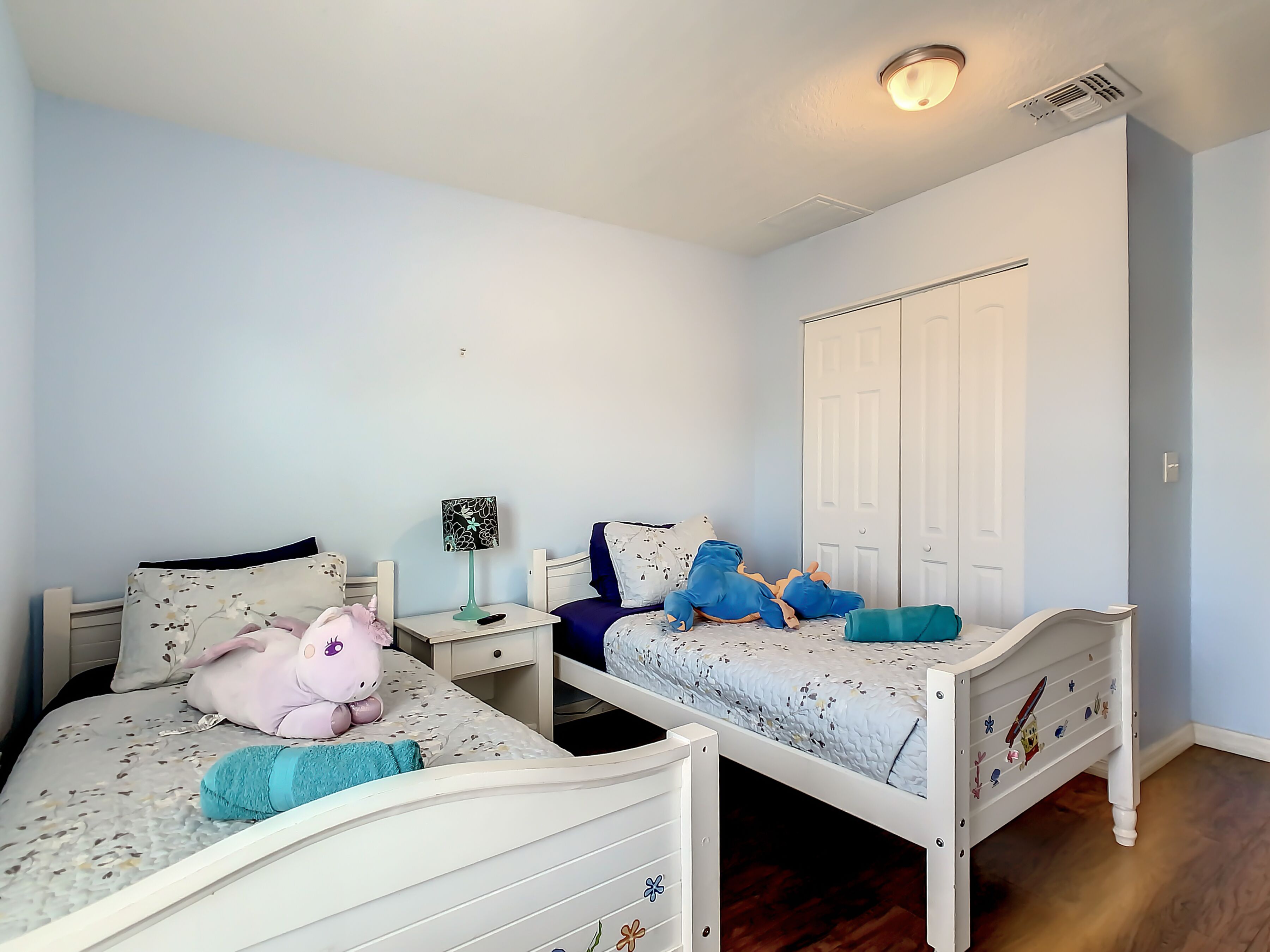 Une chambre avec deux lits simples, une table de chevet avec une lampe, une armoire et un luminaire au plafond.