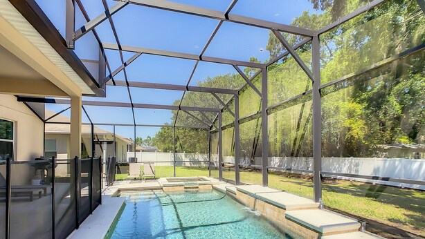 A swimming pool with a glass enclosure, surrounded by a white fence and trees. - Cost-Effectiven 8BR/5BA pool home! Near Disney,SeaWorld and Convention Ctr (Kissimmee)