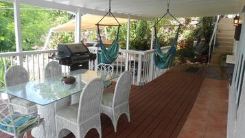 A covered outdoor patio with a glass table, white wicker chairs, a grill, and a hammock.