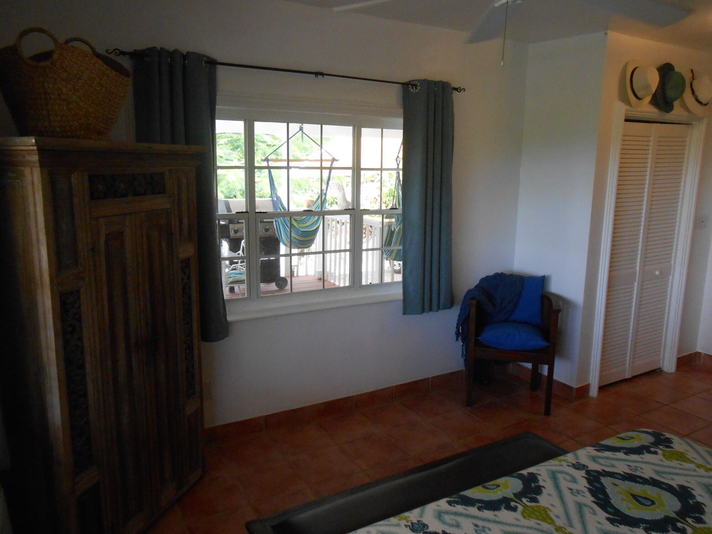 Una habitació amb un armari de fusta, una finestra amb cortines, una cadira amb coixí blau i una catifes amb dibuixos al terra.