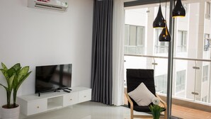 A modern living room with a flat-screen TV, a potted plant, a black chair with a white cushion, and a round table with a small plant. - Nice Apartment at GoldView (Ho Chi Minh City)