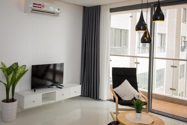 A modern living room with a flat-screen TV, a potted plant, a black chair with a white cushion, and a round table with a small plant. - Nice Apartment at GoldView (Ho Chi Minh City)