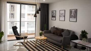 Un salon moderne avec un canapé, une table basse ronde, un fauteuil noir et une table à manger. Trois tableaux encadrés ornent le mur, une grande fenêtre est agrémentée de rideaux et un tapis à carreaux recouvre le sol.