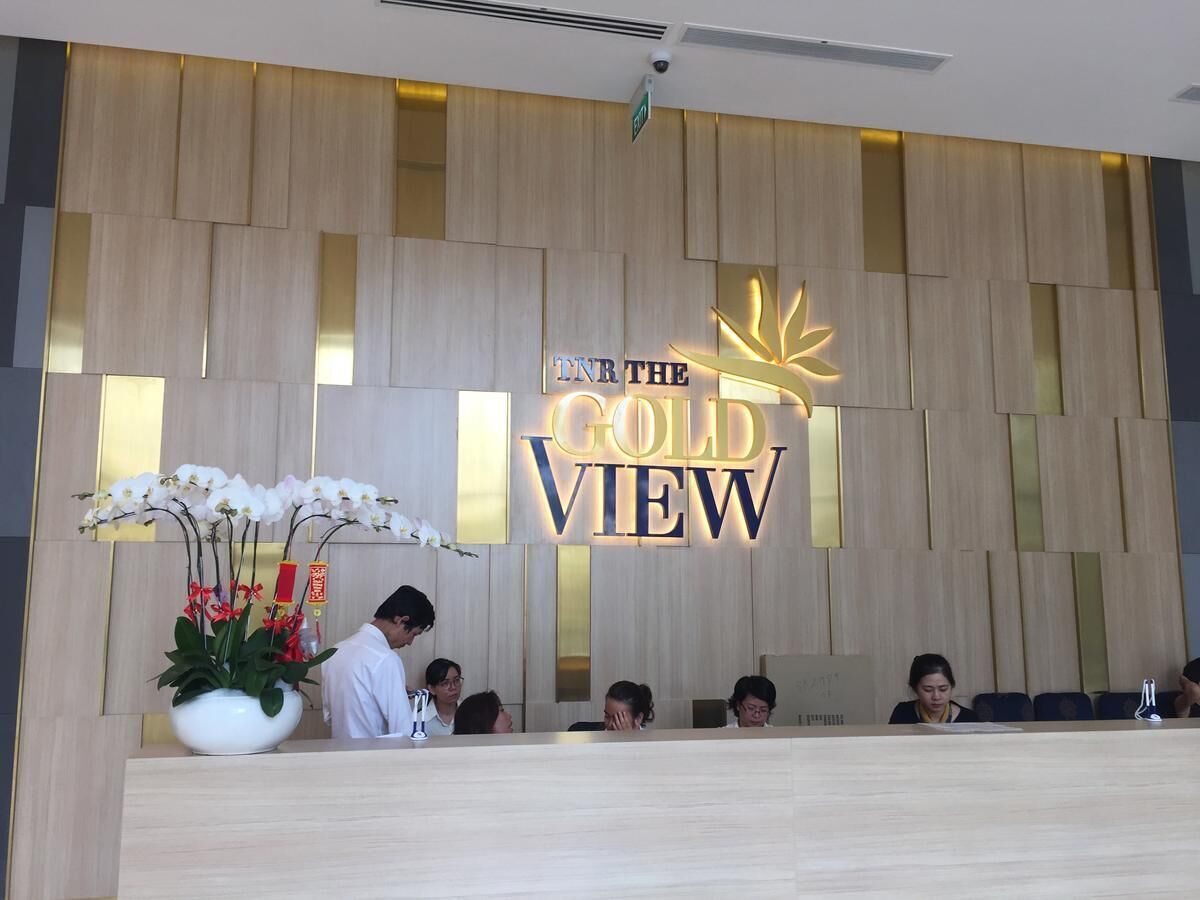 Un comptoir d’accueil avec une pancarte indiquant « IN THE GOLD VIEW » et une plante en pot ornée d’orchidées blanches.