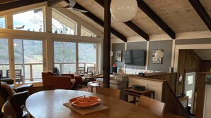 Amplia sala de estar con una gran mesa de comedor de madera, asientos cómodos y vistas a través de amplias ventanas.