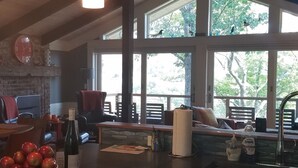 Una cocina con pared de piedra, vigas de madera en el techo, un ventanal grande y un bol de manzanas sobre la encimera.