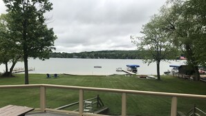 A deck with a picnic table and chairs, overlooking a lake with docks and boats. - Beautiful Walloon Lake Home - with Pontoon Boat option. Sept & Oct availability! (Petoskey)