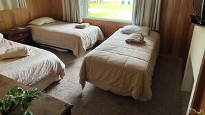 A hotel room with two beds, a wooden floor, a window with curtains, and a small bedside table. - Beautiful Walloon Lake Home - with Pontoon Boat option. Sept & Oct availability! (Petoskey)