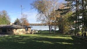 A lakeside property with a small cabin, a dock, and a grassy area. - Beautiful Walloon Lake Home - with Pontoon Boat option. Sept & Oct availability! (Petoskey)