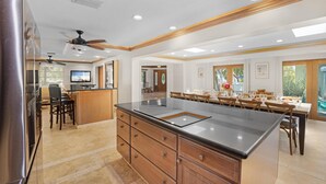 A spacious kitchen with a central island, wooden cabinetry, and a dining area with a large table and chairs. - Elegant Home with Beach & Dockage! Spectacular Sunsets! (Key Largo)