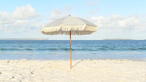 Una sombrilla en una playa arenosa, con el océano y una isla distante al fondo.