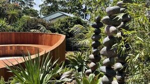 Un jardín con un banco de madera, diversas plantas y una pila de piedras.