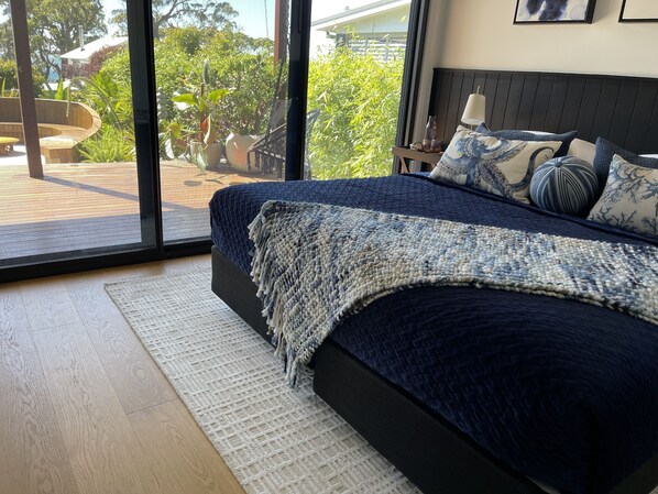 A modern bedroom with a large bed, a view of the outdoors, and a wooden deck. - Luxury Beach House - Book 2 nights and get 1 night FREE T & C's apply (Hyams Beach)