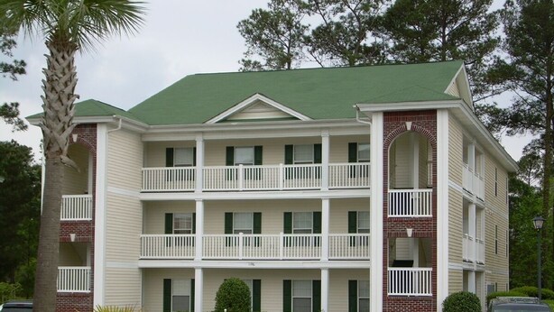 A multi-story hotel with a green roof, white balconies, and a brick facade. - First Floor Luxury 1,350 Sq Ft  First Floor Condo w/ No Steps  (Myrtle Beach)