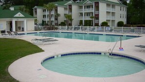 A pool area with a circular hot tub, lounge chairs, and a building with multiple balconies in the background. - First Floor Luxury 1,350 Sq Ft  First Floor Condo w/ No Steps  (Myrtle Beach)