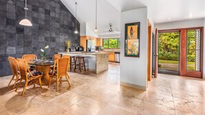 Una cocina moderna con una isla grande, comedor con sillas de mimbre y vista a un jardín exuberante a través de una puerta corredera.
