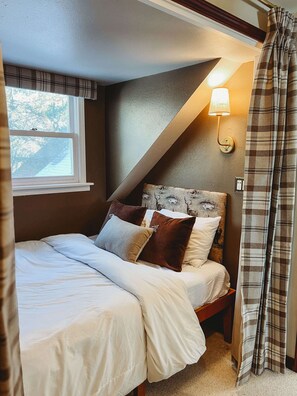 Un dormitorio con cama, almohadas, lámpara y ventana.
