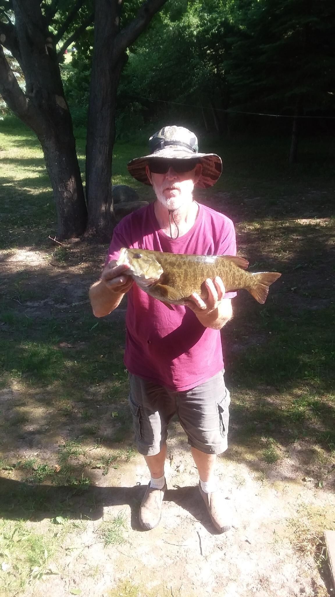 Une personne tenant un poisson à l’extérieur, avec des arbres en arrière-plan.