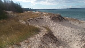 Une plage de sable avec des dunes et une étendue d’eau en arrière-plan.