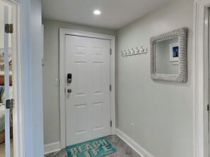 A hallway with a white door, a wall-mounted mirror, and a 'BEACH LIFE' mat.