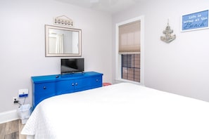 Een slaapkamer met een bed, een blauwe dressoir, een televisie, een raam met zonwering en een decoratie aan de muur.