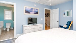 Une chambre à coucher avec un lit, un téléviseur posé sur une commode, une chaise et une porte donnant sur une autre pièce.