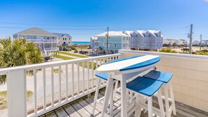 Un balcon avec une table et des chaises donnant sur une plage, avec des bâtiments en arrière-plan.