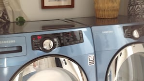 A Samsung washing machine with a control panel, a framed picture on the wall, and baskets on a shelf. - WALK to Lake Michigan AND Saugatuck ~ Includes Bicycles! (Douglas)