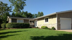 A single-story house with a front garage, a well-maintained lawn, and a stone foundation. - WALK to Lake Michigan AND Saugatuck ~ Includes Bicycles! (Douglas)
