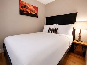 A neatly made bed with white linens, a black headboard, and a single decorative pillow. - Barrel Sauna, HotTub, 2 Zero Gravity Massage Chairs, Powder Gong, Arcade & more (Revelstoke)
