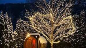 A wooden cabin with a circular design, surrounded by snow-covered trees and a mountain backdrop.