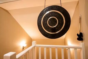 A staircase with a hanging circular object, a white railing, and a wall-mounted light fixture. - Barrel Sauna, HotTub, 2 Zero Gravity Massage Chairs, Powder Gong, Arcade & more (Revelstoke)