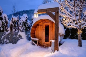 Ein hölzernes, mit Schnee bedecktes Gebäude mit Tür und Bank vor der Fassade.