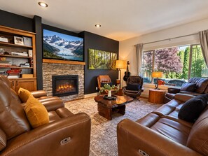 A living room with leather sofas, a fireplace, a television, and a large window with a view of trees.