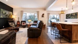 A spacious living room with a sofa, ottoman, and a dining area with bar stools.