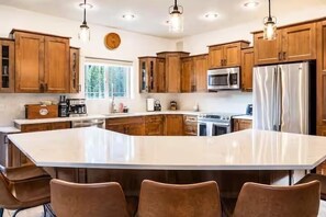 A kitchen with wooden cabinets, stainless steel appliances, and a large island with bar stools. - Barrel Sauna, HotTub, 2 Zero Gravity Massage Chairs, Powder Gong, Arcade & more (Revelstoke)