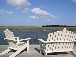 Two white Adirondack chairs on a wooden dock by a calm body of water with a clear sky and distant trees. - Savannah Whitemarsh Island Cottage on Private Riverfront Estate with Dock
 (Savannah)