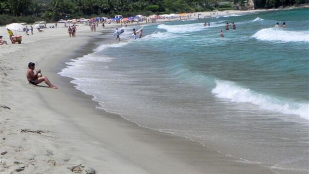 A beach with people swimming and sunbathing, a sandy shore, and a forested hillside in the background. - Nice house just 330 feet away from the beach (São Sebastião)