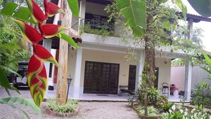A two-story house with a balcony, surrounded by tropical plants and a gravel driveway. - Nice house just 330 feet away from the beach (São Sebastião)